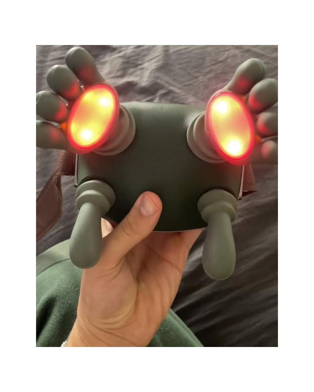 Hand holding a shiatsu massaging device with red lights and green handles. by daily relief co